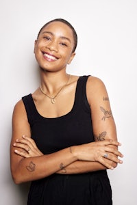 a young woman with tattoos smiling in front of a white wall